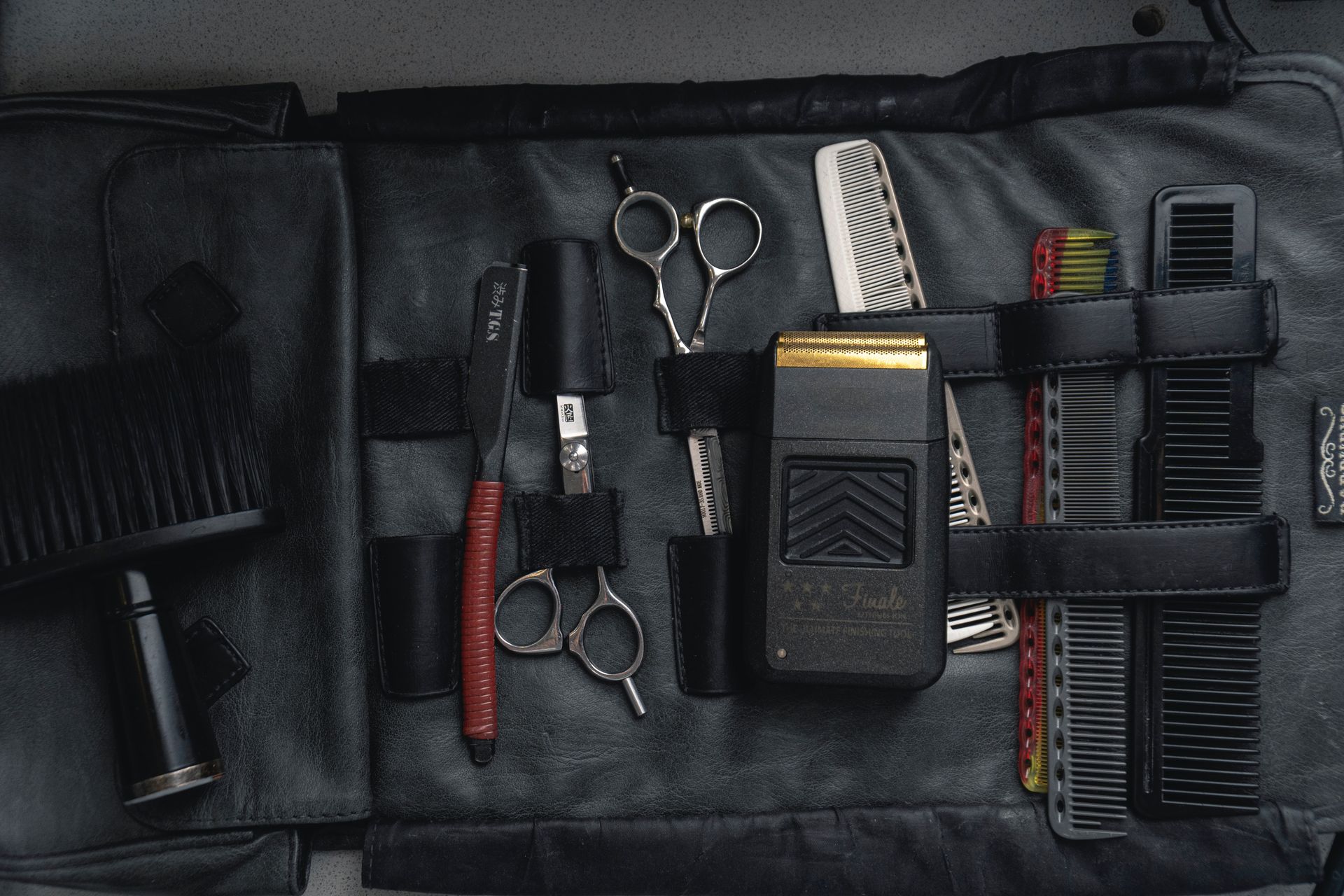 Barber tools in a black leather case: scissors, razor, clippers, combs, and brush.