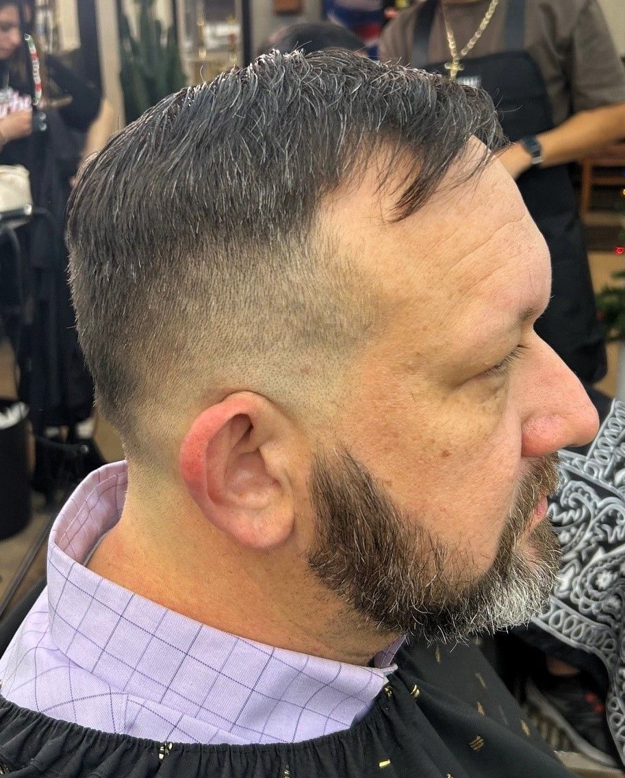 Man with faded haircut and beard at a barber shop, wearing a purple collared cape.