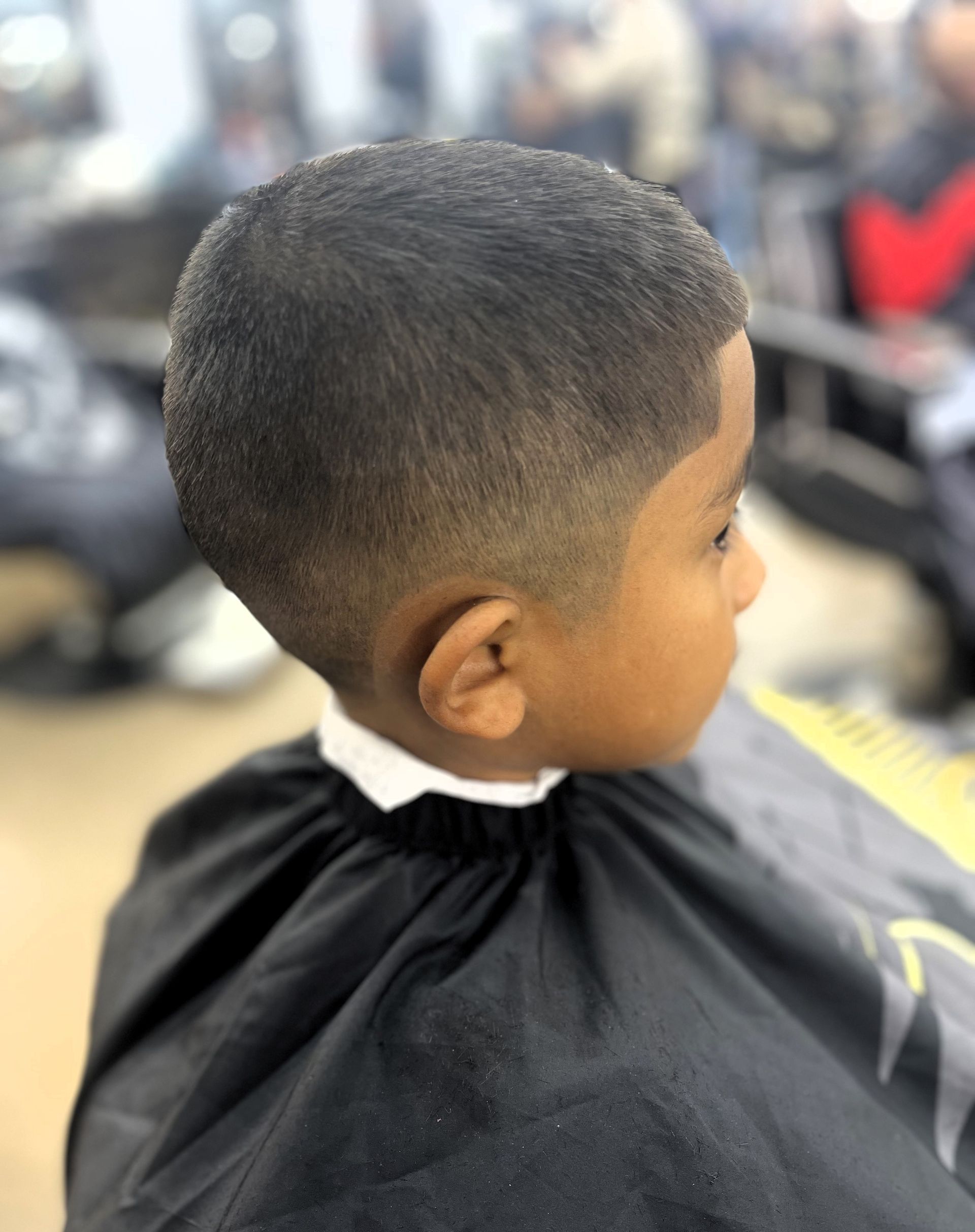 Boy getting a haircut at a barbershop; close-up of the back of his head with short, faded hair, wearing a barber's cape.