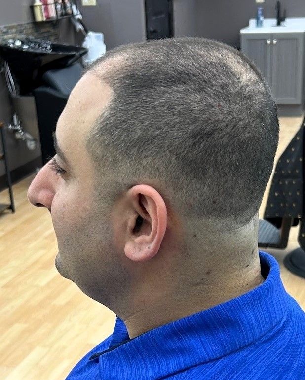Man with short, faded haircut, side profile view, in a salon, wearing a blue shirt.