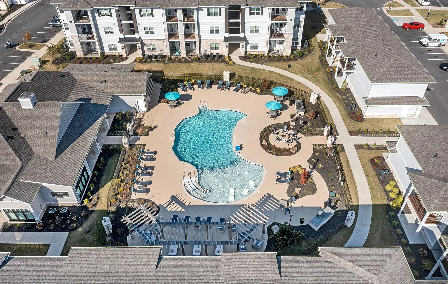 Aerial view of a residential community pool with loungers, umbrellas, and surrounding apartment buildings at Graces Reserve Apartments in Kannapolis, NC.