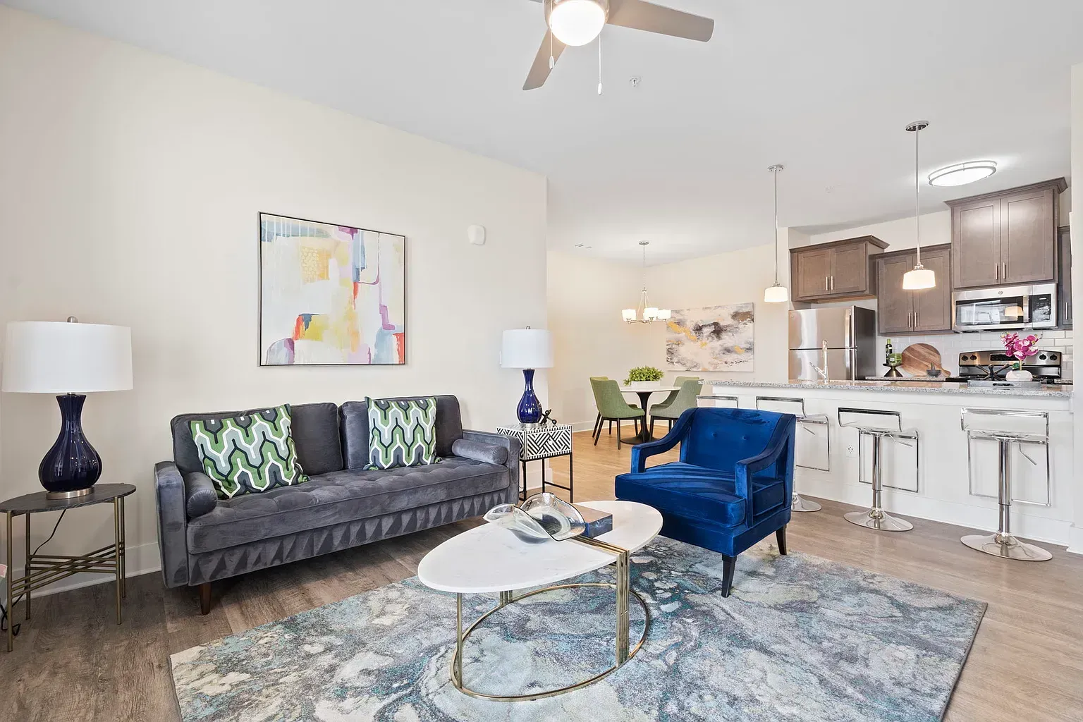 Open-concept living area in a modern apartment with gray sofa, blue velvet chair, and kitchen island at Graces Reserve Apartments in Kannapolis, NC.