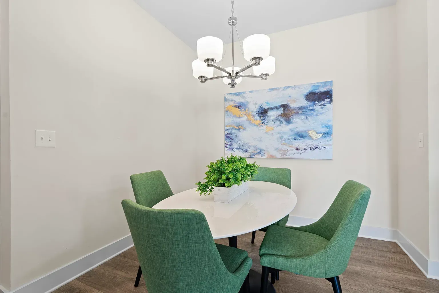 Dining nook with a white round table, four green upholstered chairs, and a modern chandelier at Graces Reserve Apartmentsin Kannapolis, NC.