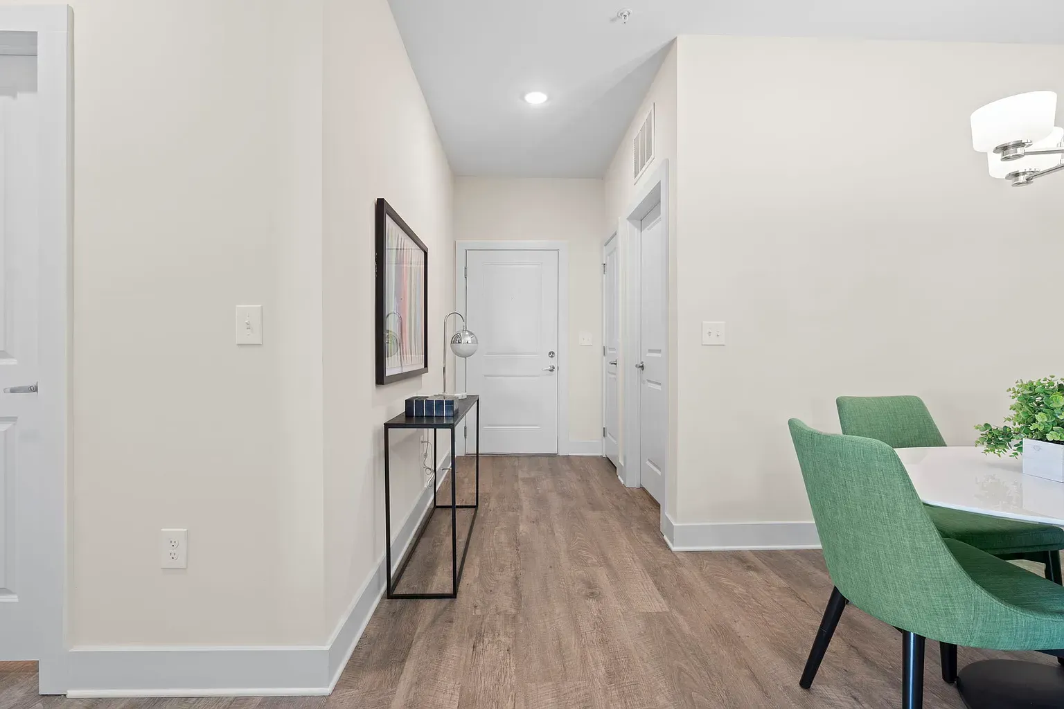 Interior apartment hallway with a console table, wall art, and a dining area with green chairs at Graces Reserve Apartments in Kannapolis, NC.