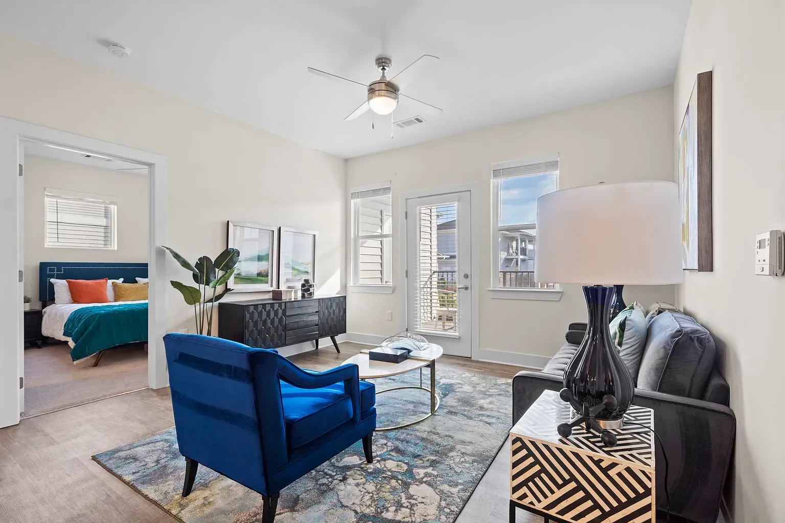 Bright living room in an apartment with a blue accent chair, gray sofa, and doorway to bedroom at Graces Reserve Apartments in Kannapolis, NC.
