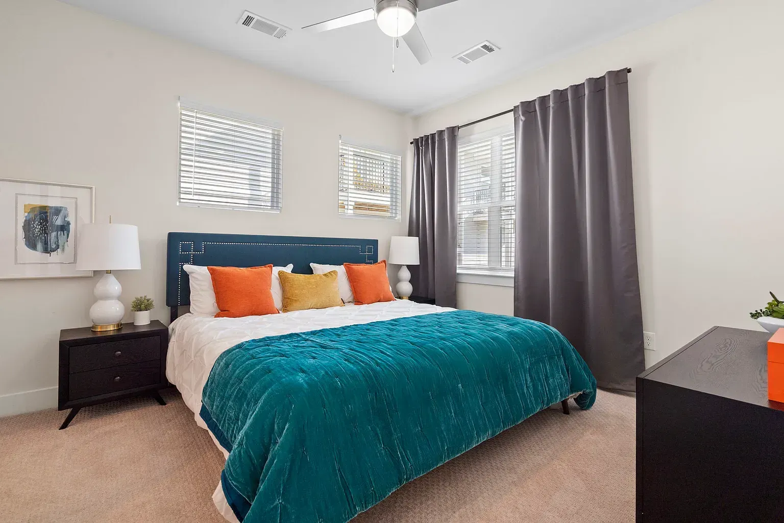 Bright bedroom with teal upholstered headboard, white bedding, and gray curtains at Graces Reserve Apartments in Kannapolis, NC.