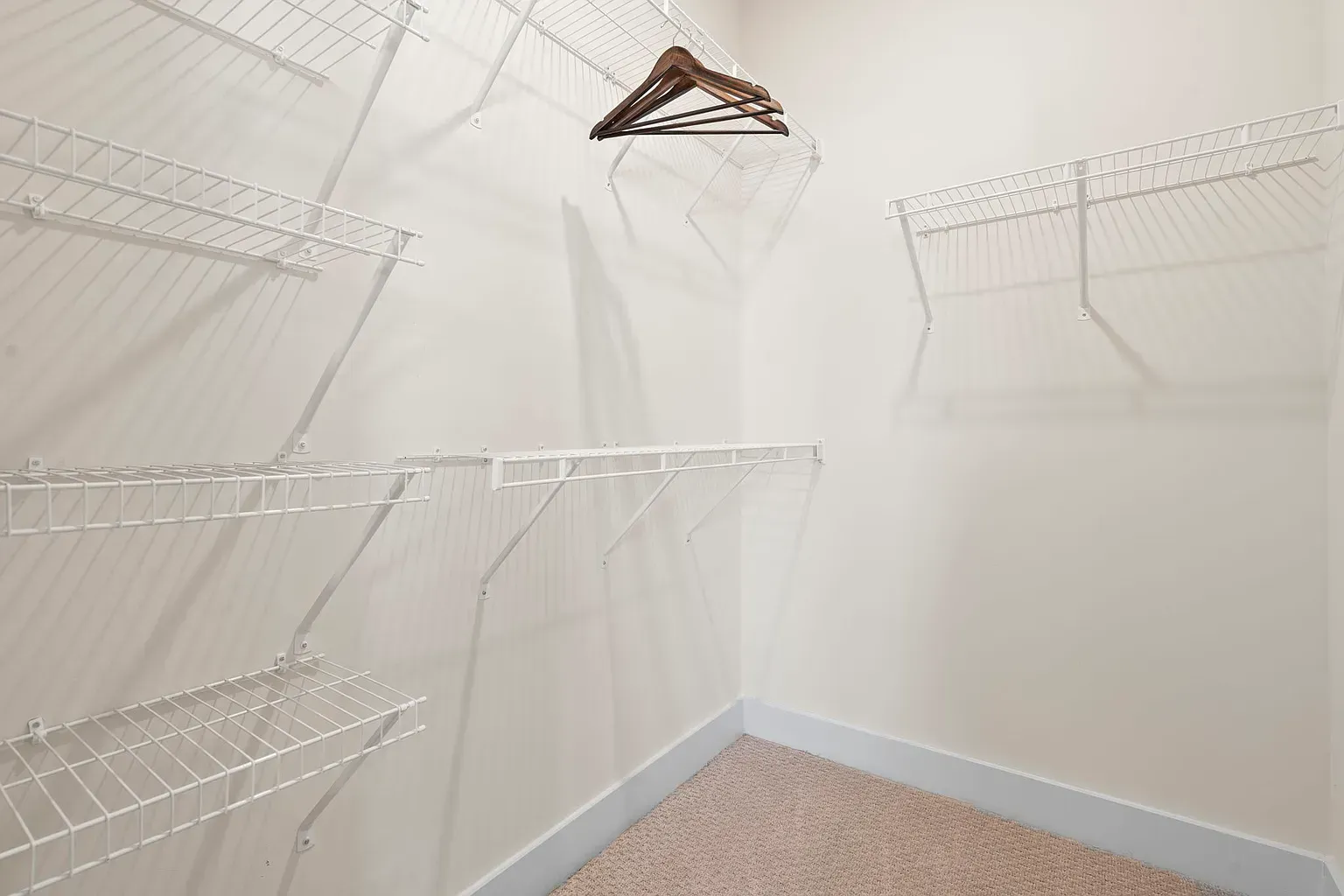 Walk-in closet with white wire shelving and hanging rods, beige carpet at Graces Reserve Apartments in Kannapolis, NC.