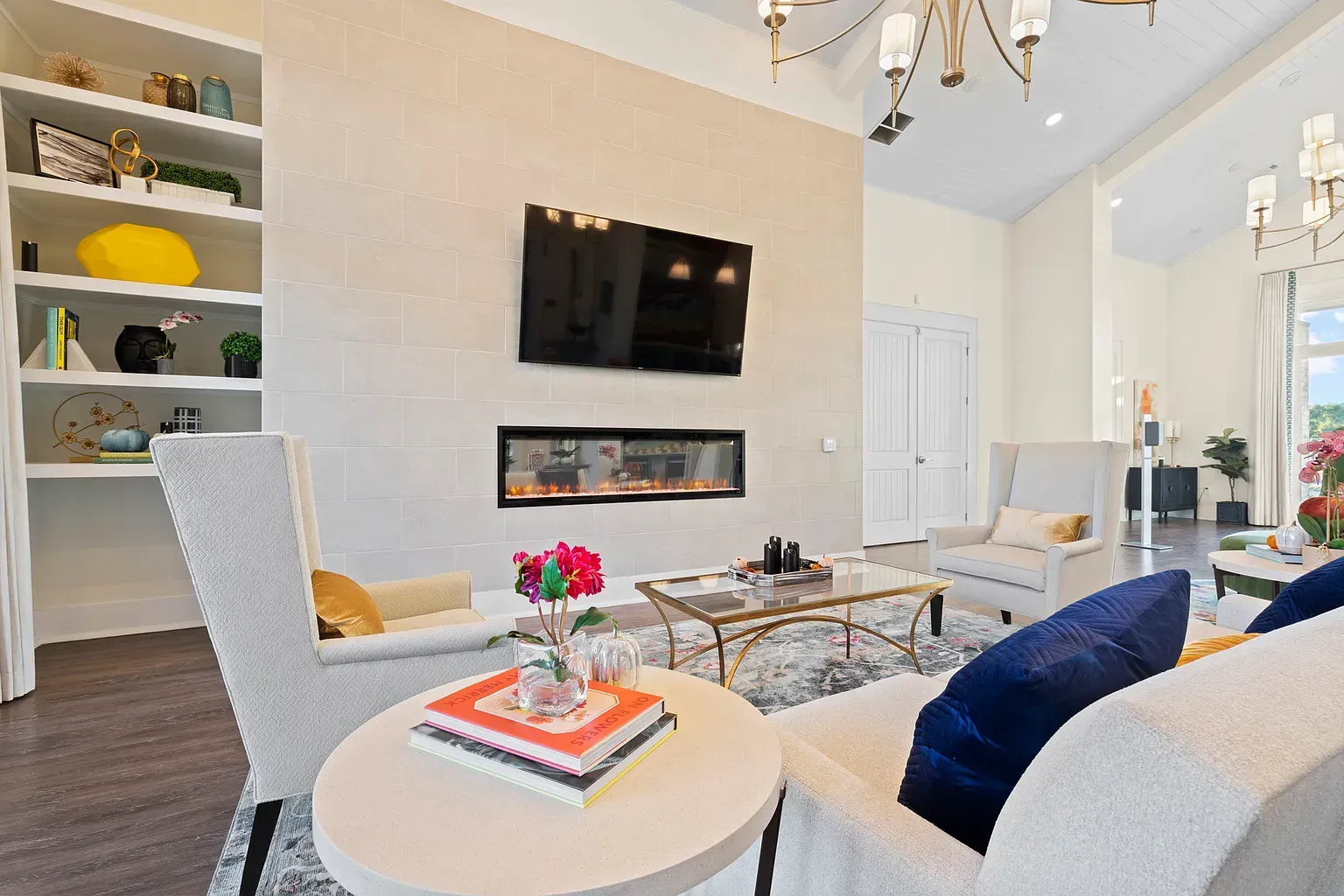 Bright lounge with a wall-mounted TV above a linear fireplace, white seating, and built-in shelves at Graces Reserve Apartments in Kannapolis, NC.