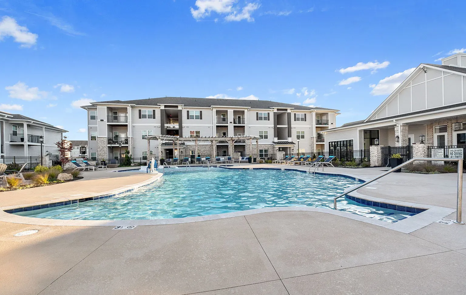 Outdoor apartment community pool with lounge chairs and a pergola, building in the background at Graces Reserve Apartments in Kannapolis, NC.