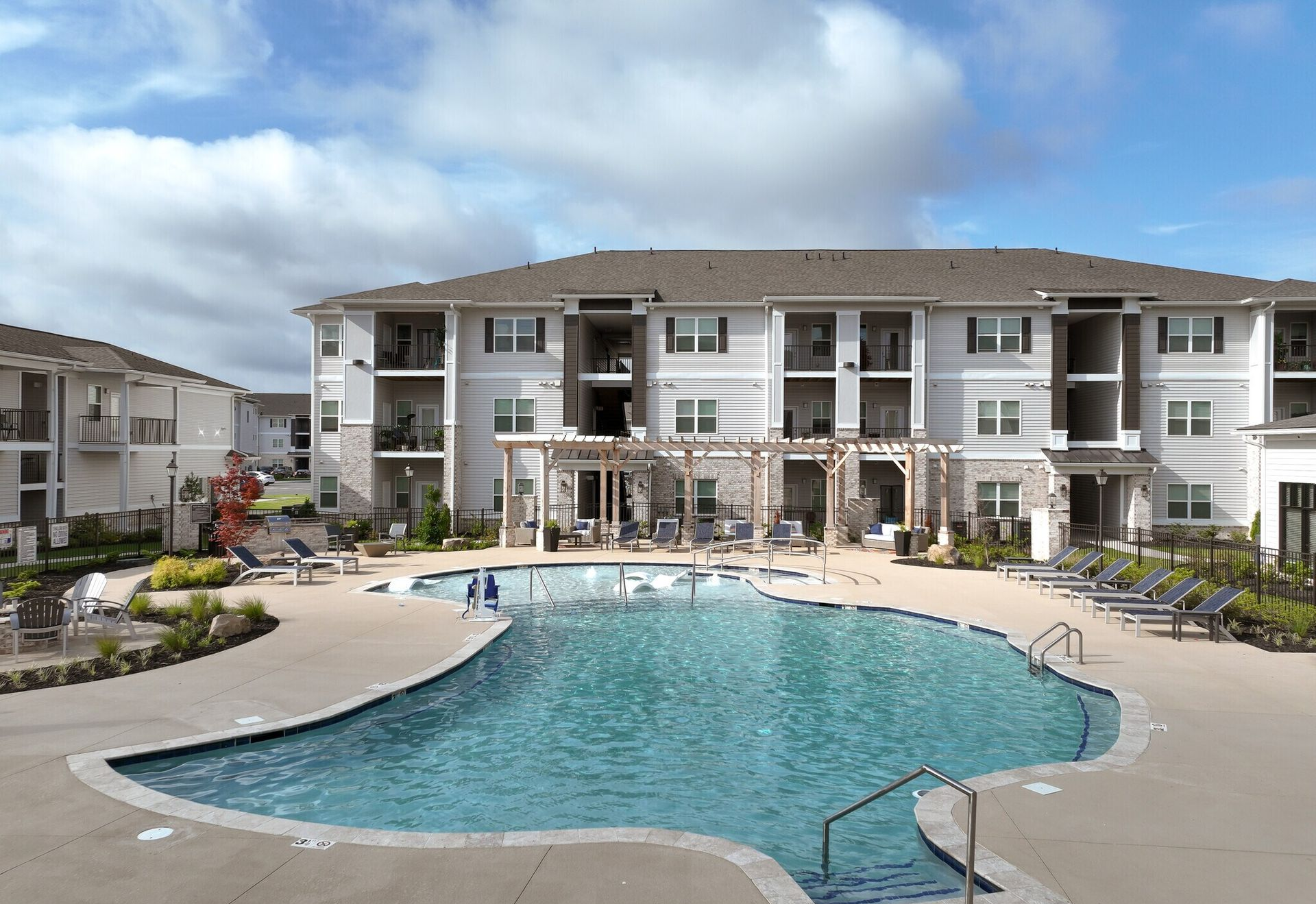 Apartment complex with pool; blue water, light-colored buildings, blue sky.