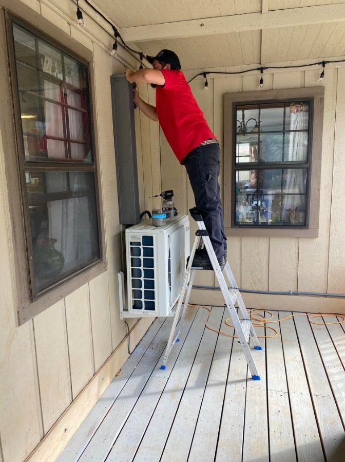 A man standing on a ladder working on an air conditioner