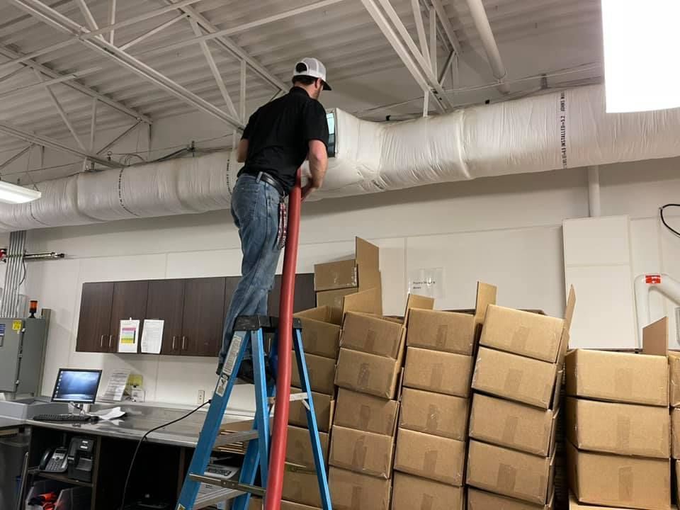 A man is standing on a ladder in front of a stack of cardboard boxes.
