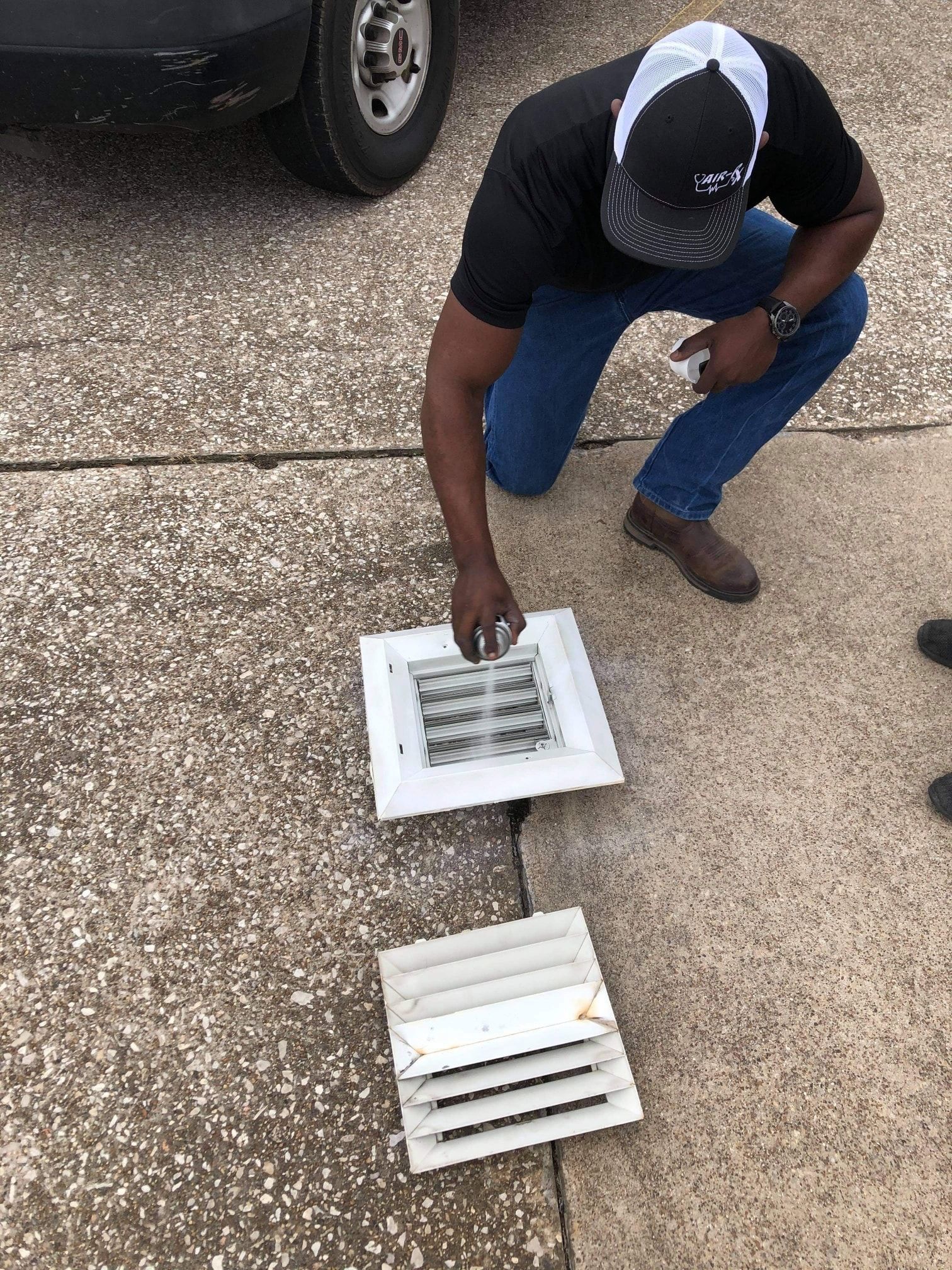 A man is kneeling down on the sidewalk next to a vent.