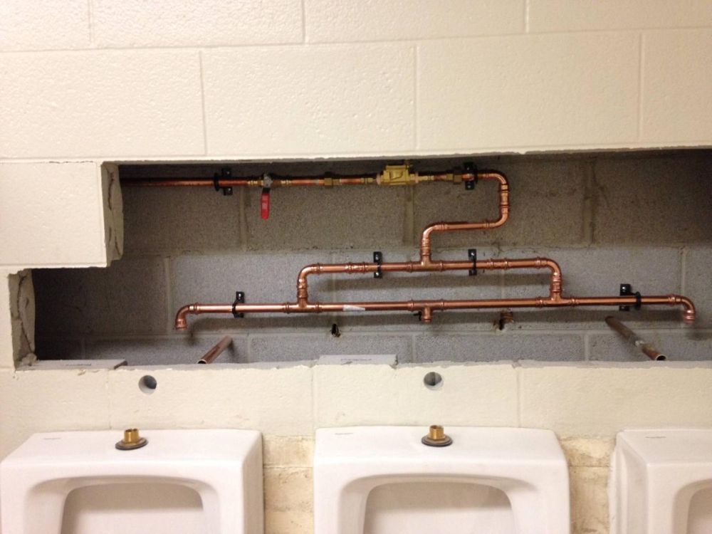 A bathroom with three urinals and copper pipes