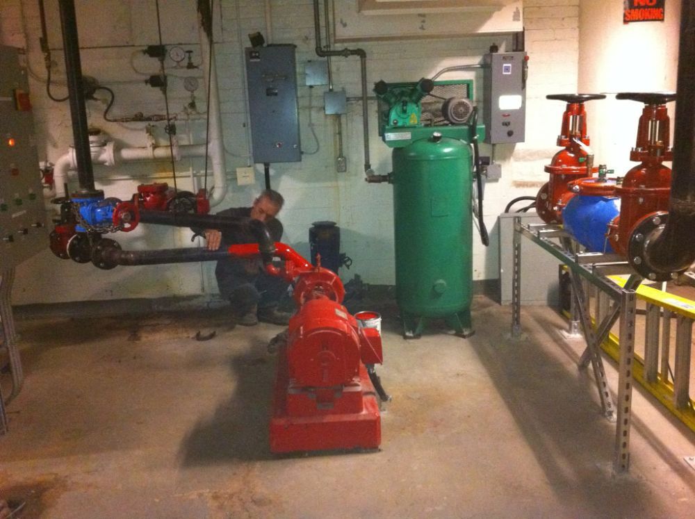 A man is working on a red pump in a room with a green tank
