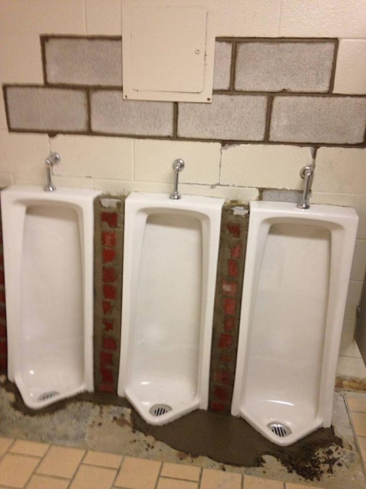 Three urinals in a bathroom with a brick wall behind them