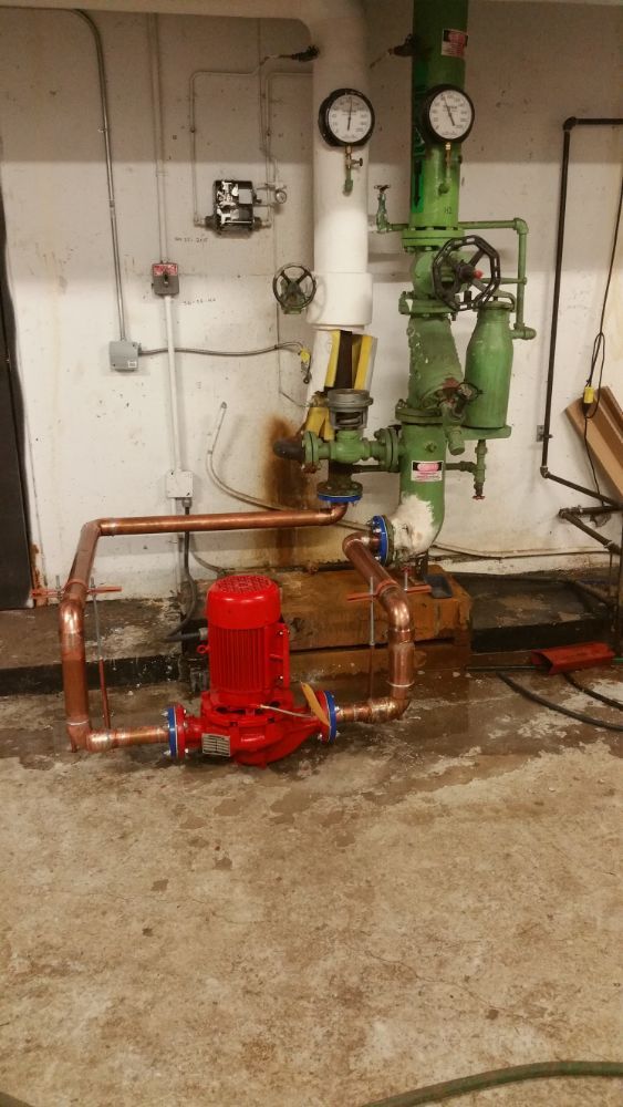 A red pump is sitting in a room next to a green pipe.