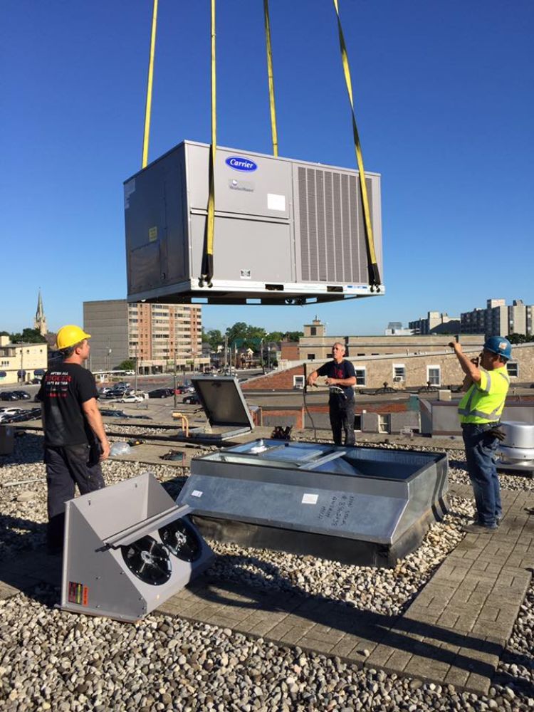 A crane is lifting a large air conditioner on top of a building.