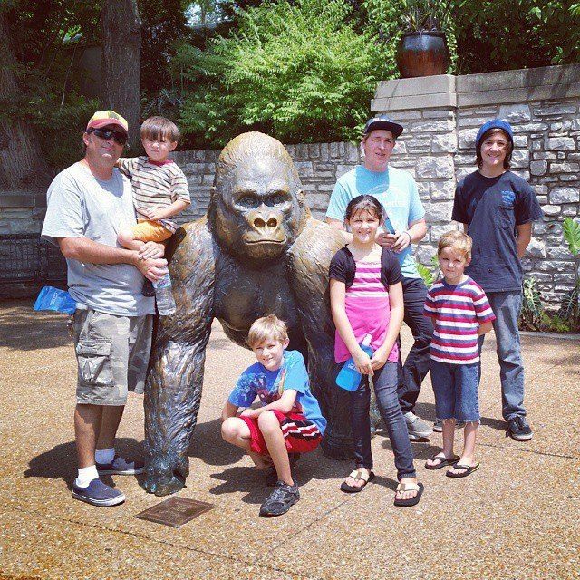 Family poses with a gorilla statue outdoors in a park.