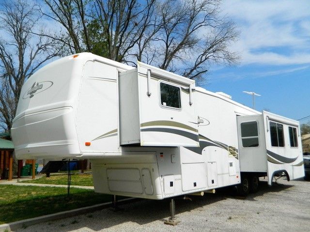 A white rv is parked in a parking lot with trees in the background