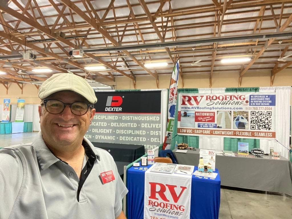 A man is taking a selfie in front of a booth at a convention.
