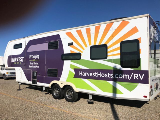 A harvest hosts trailer is parked in a gravel lot