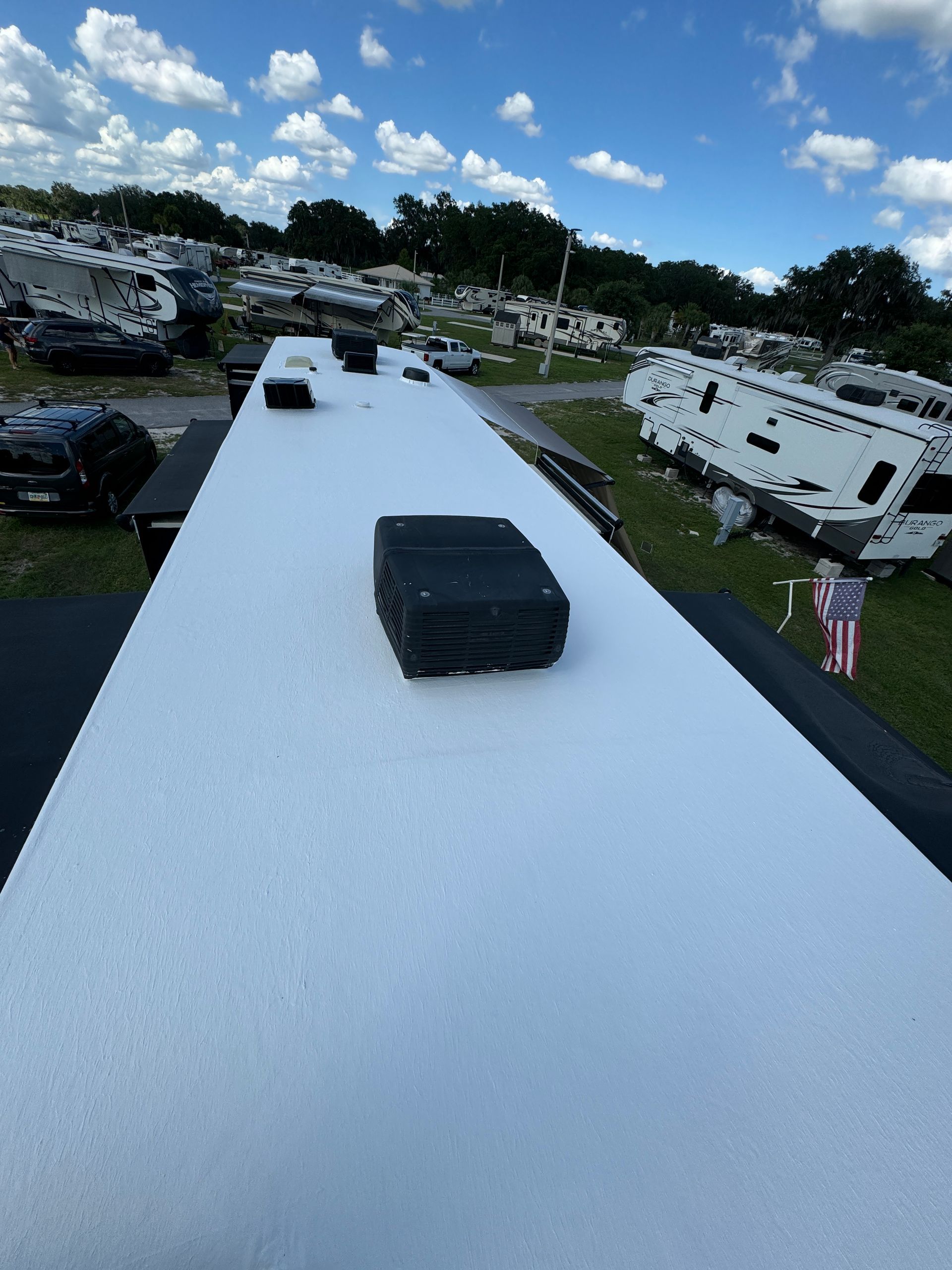 White RV roof with black vents in a crowded campground under a blue sky