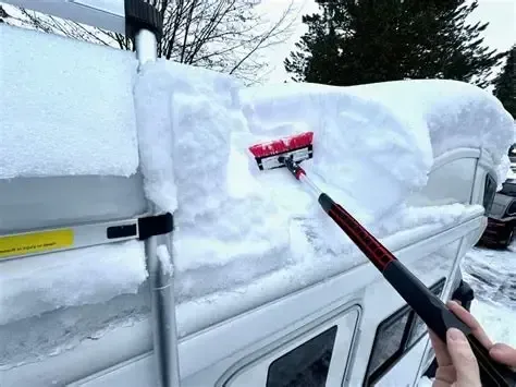 Person removing snow from the roof of a vehicle with a snow brush; snowy outdoor setting.