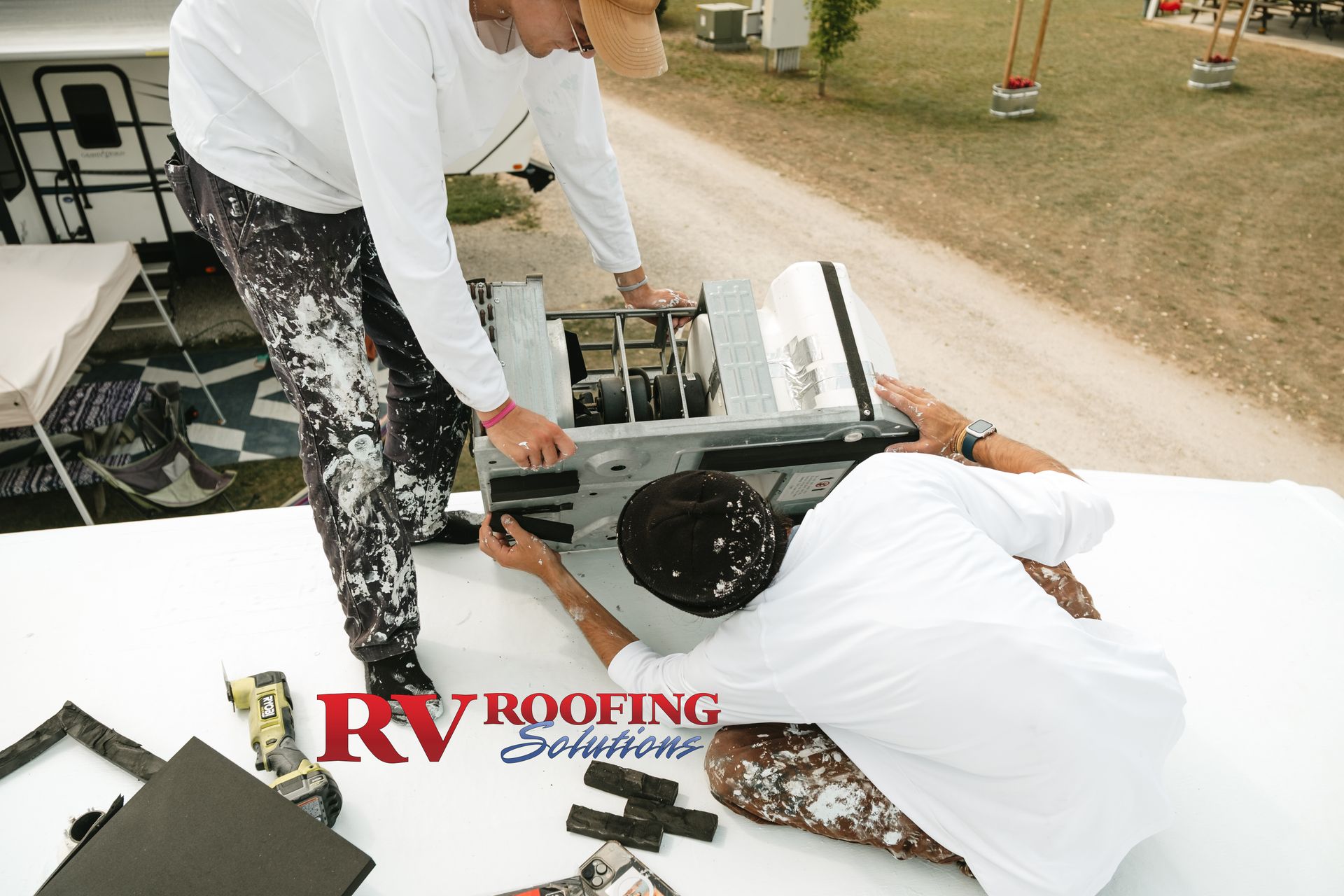 Two people installing an RV roof vent on a white RV roof outdoors.
