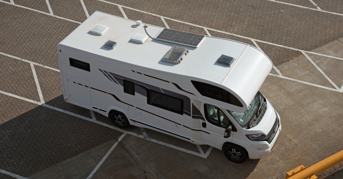 Top-down view of a mobile RV in an empty parking lot. There are hatches and vents on the RV's roof.