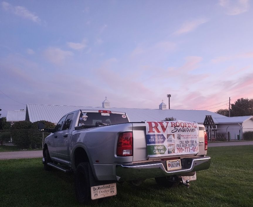 A silver truck with a sign on the back that says RV Roofing Solutions