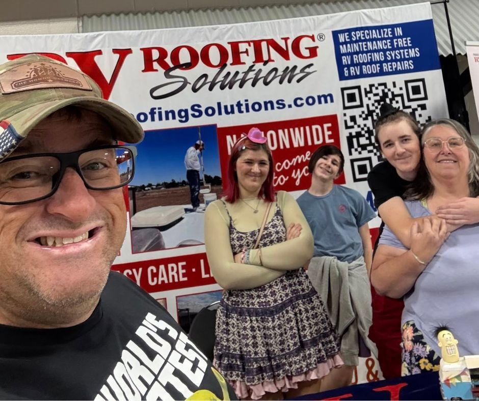 People at an RV Roofing Solutions booth; man smiling at the front, others stand behind a banner with company info.