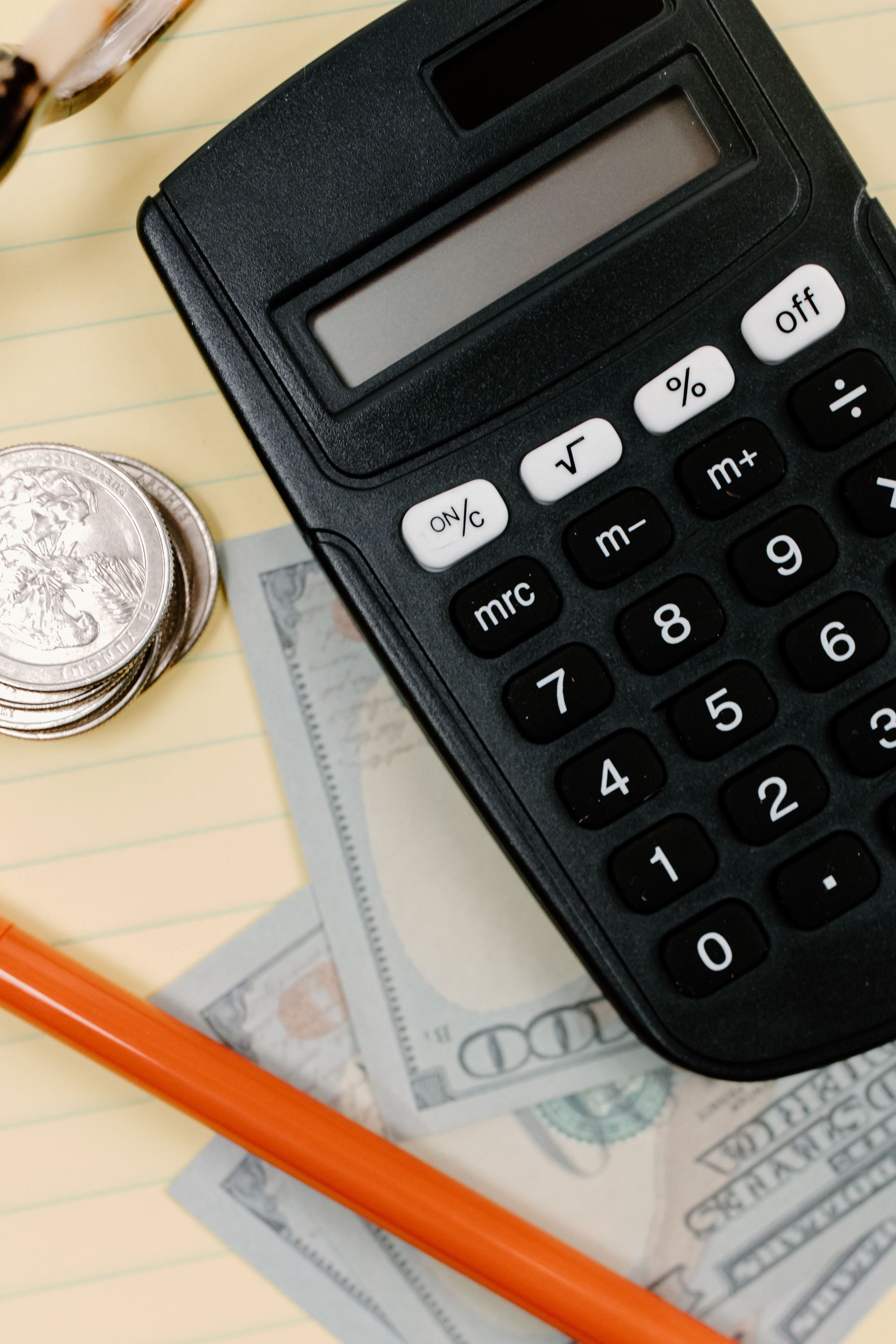 Calculator on dollar bills with a coin and pencil nearby.