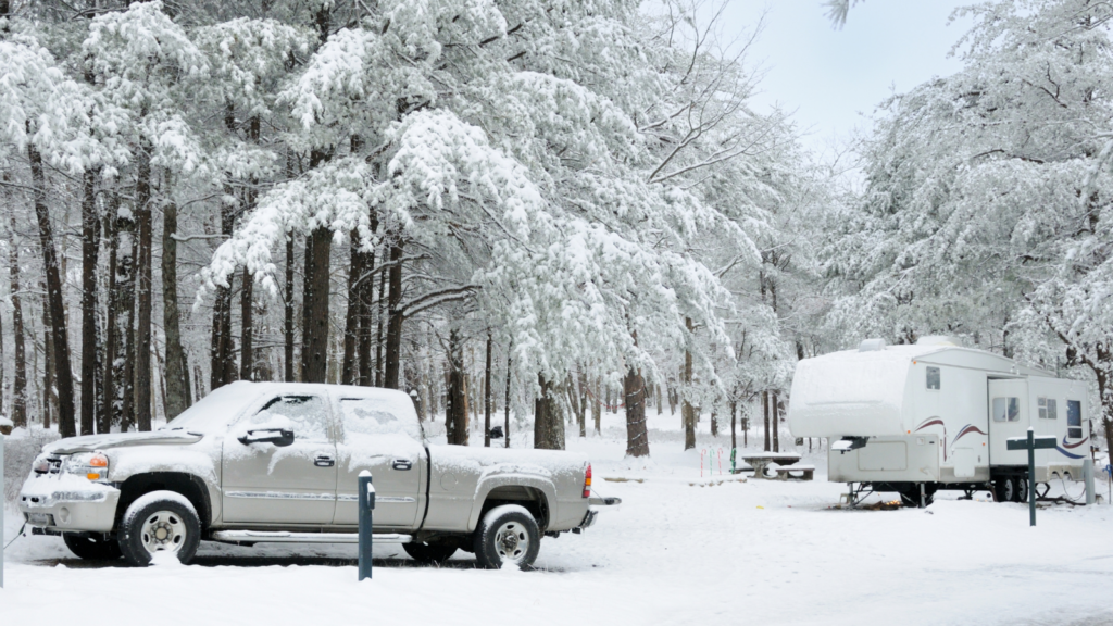 Silver truck and RV parked in snowy campground, trees covered in snow; winter camping