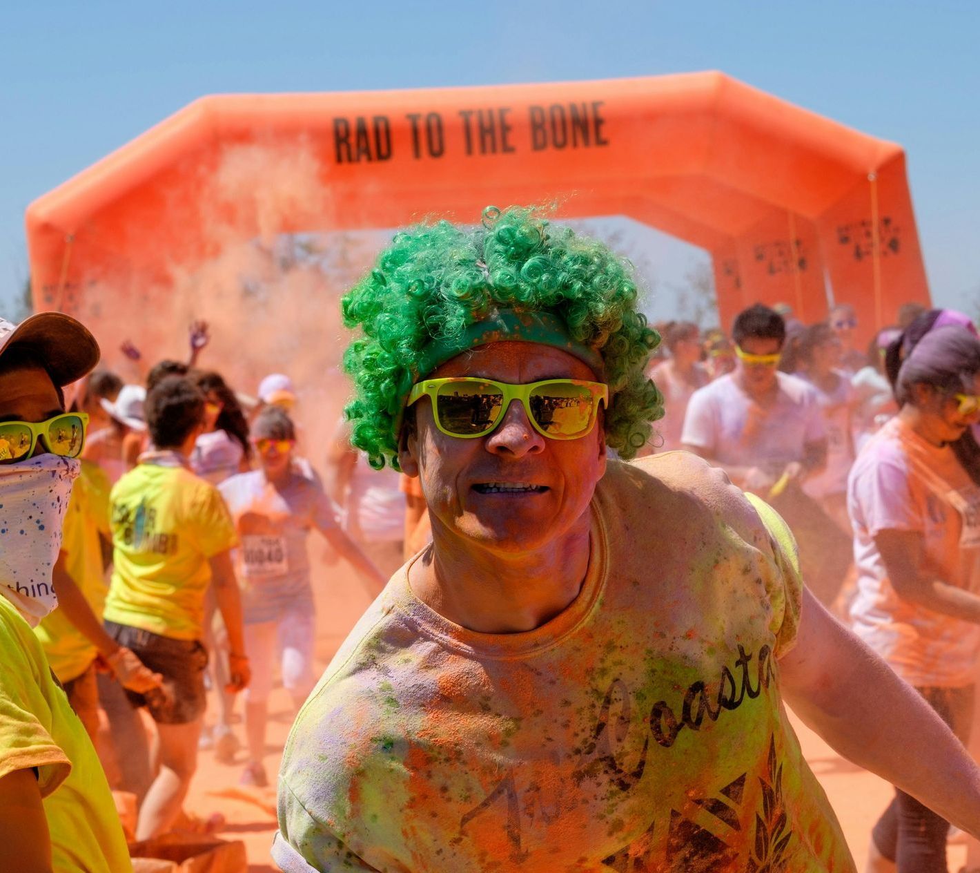 A woman with green hair and sunglasses stands in front of an inflatable sign that says rad to the bone