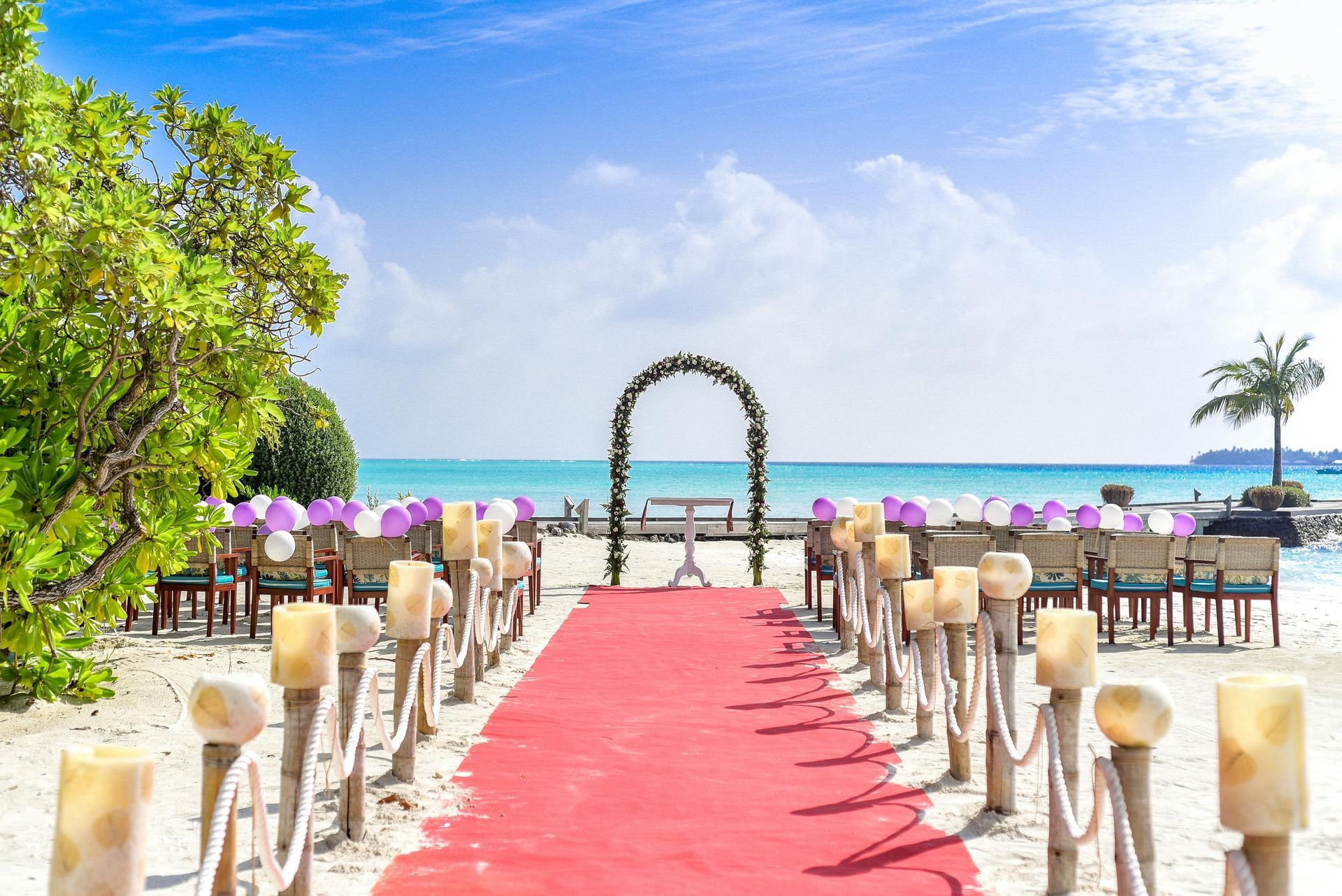 A wedding ceremony on the beach with a red carpet and candles.