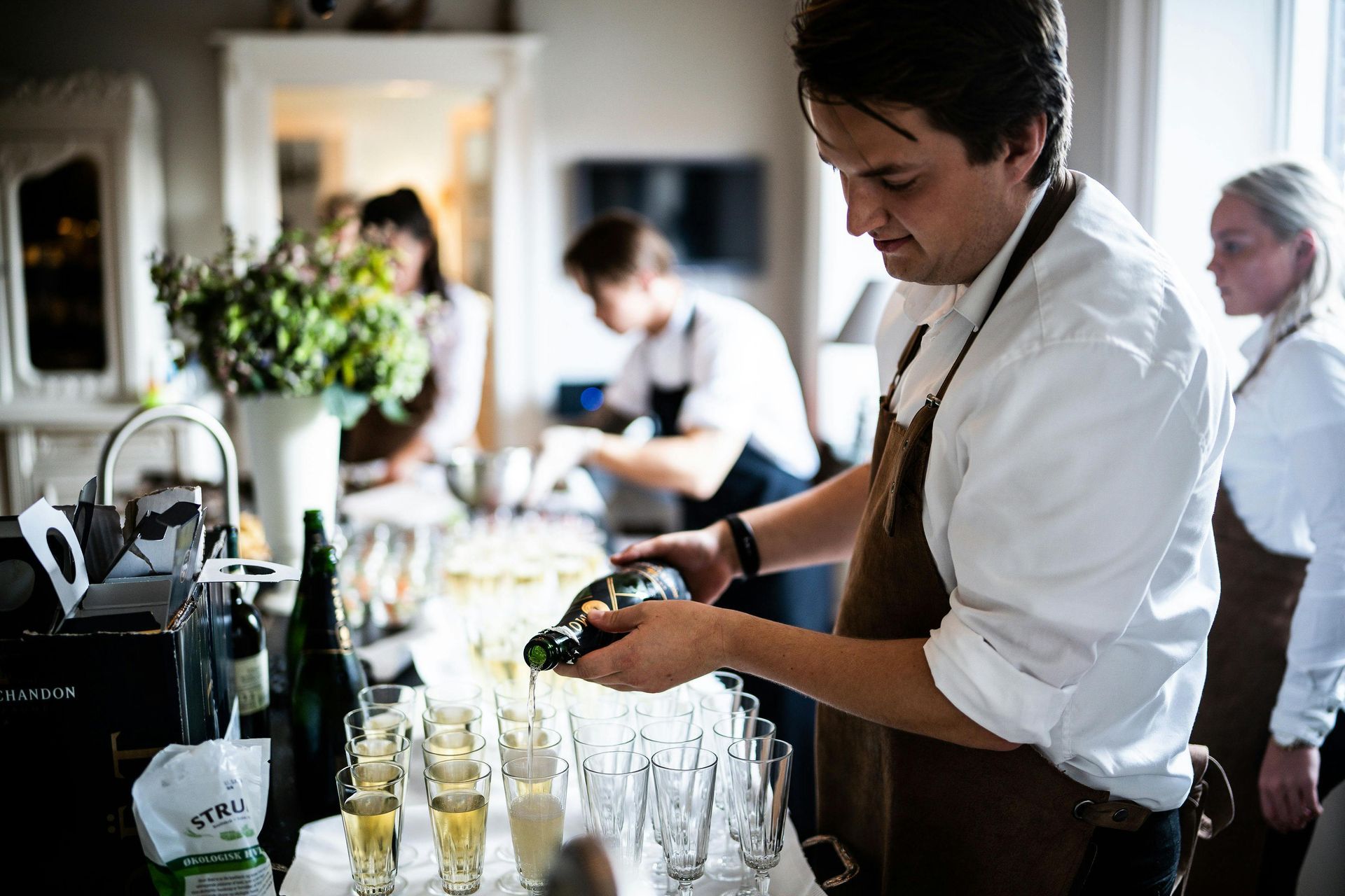 A man is pouring champagne into glasses at a bar.