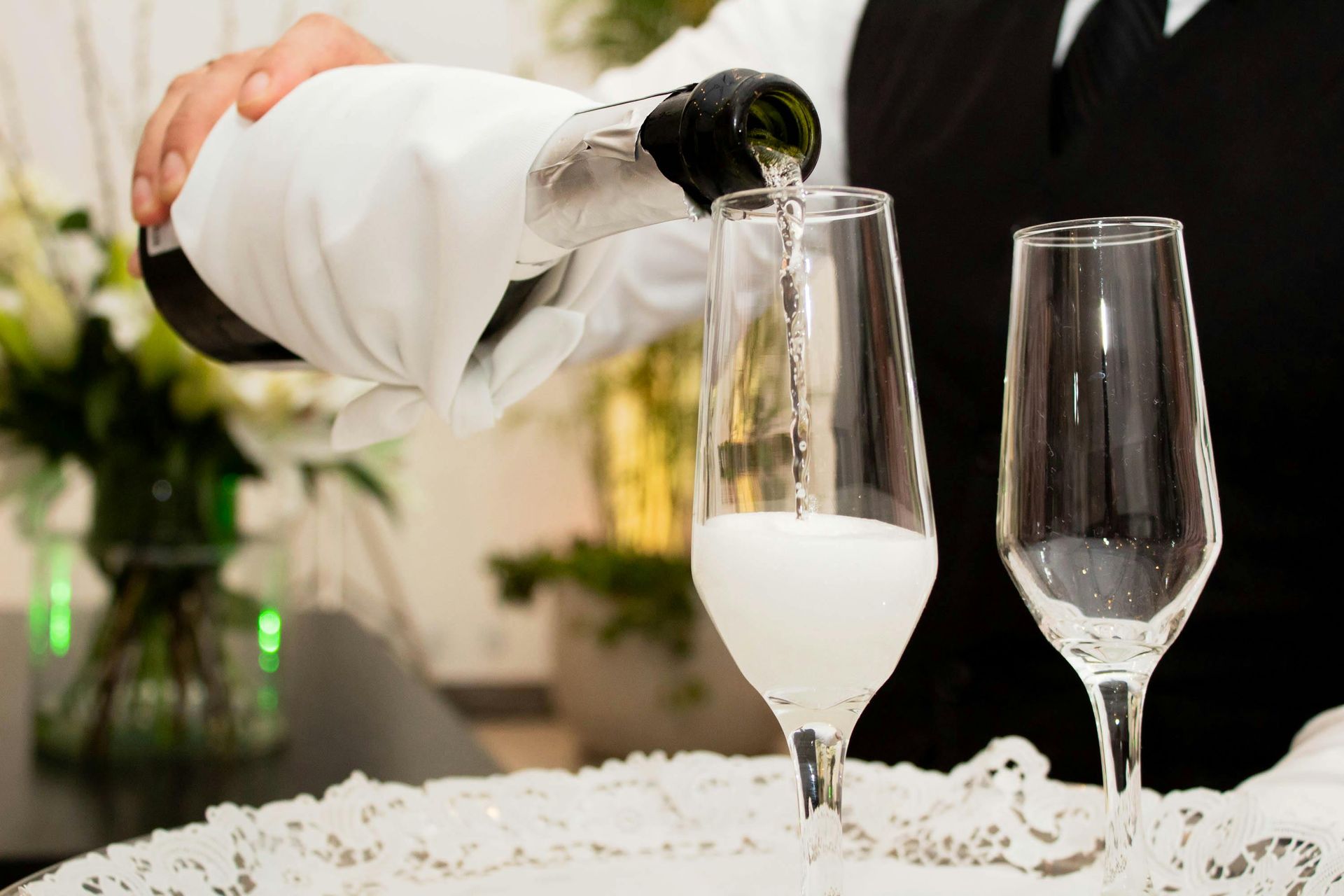 A waiter is pouring champagne into two glasses on a table.