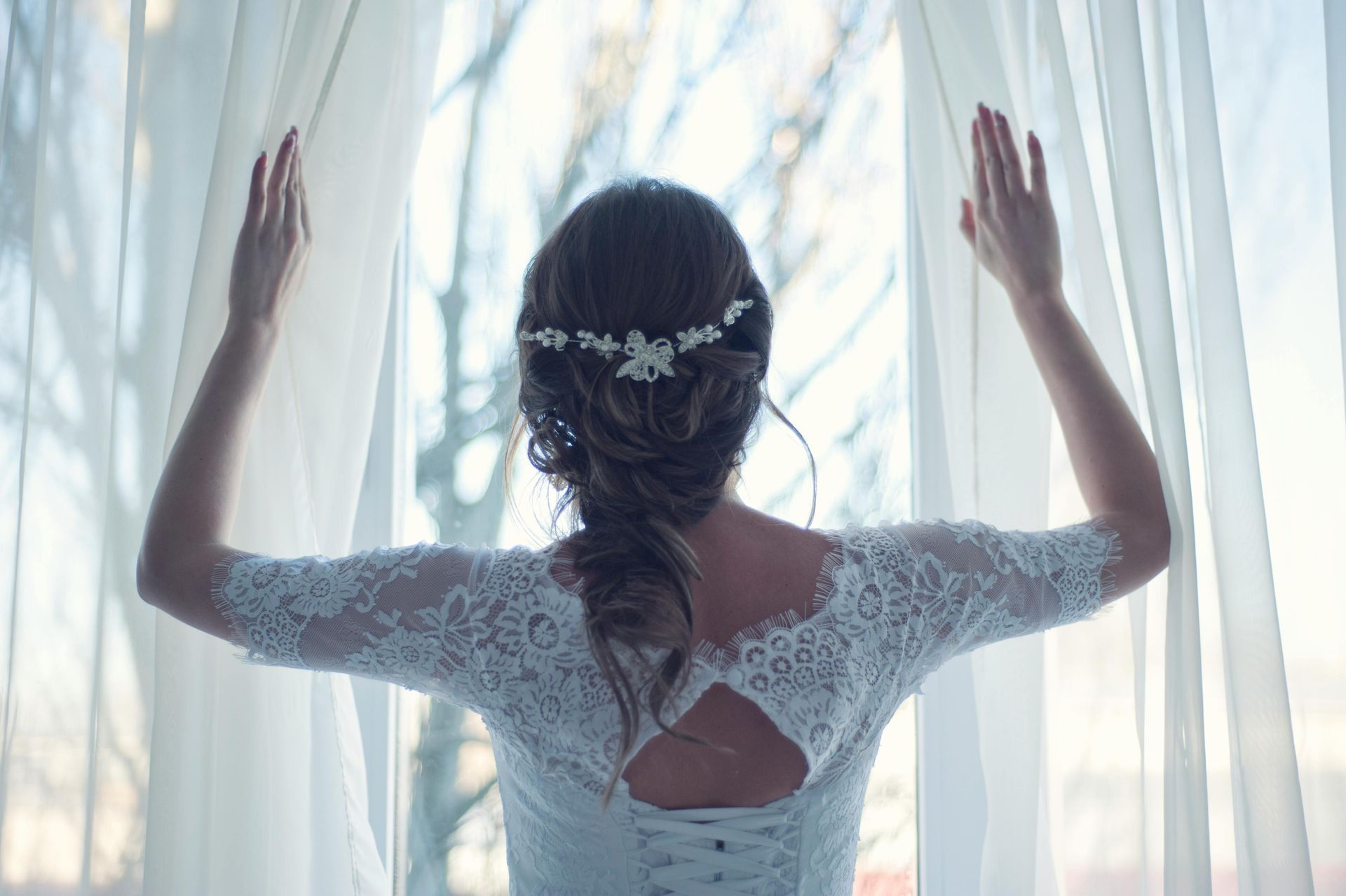 A bride in a wedding dress is looking out of a window.