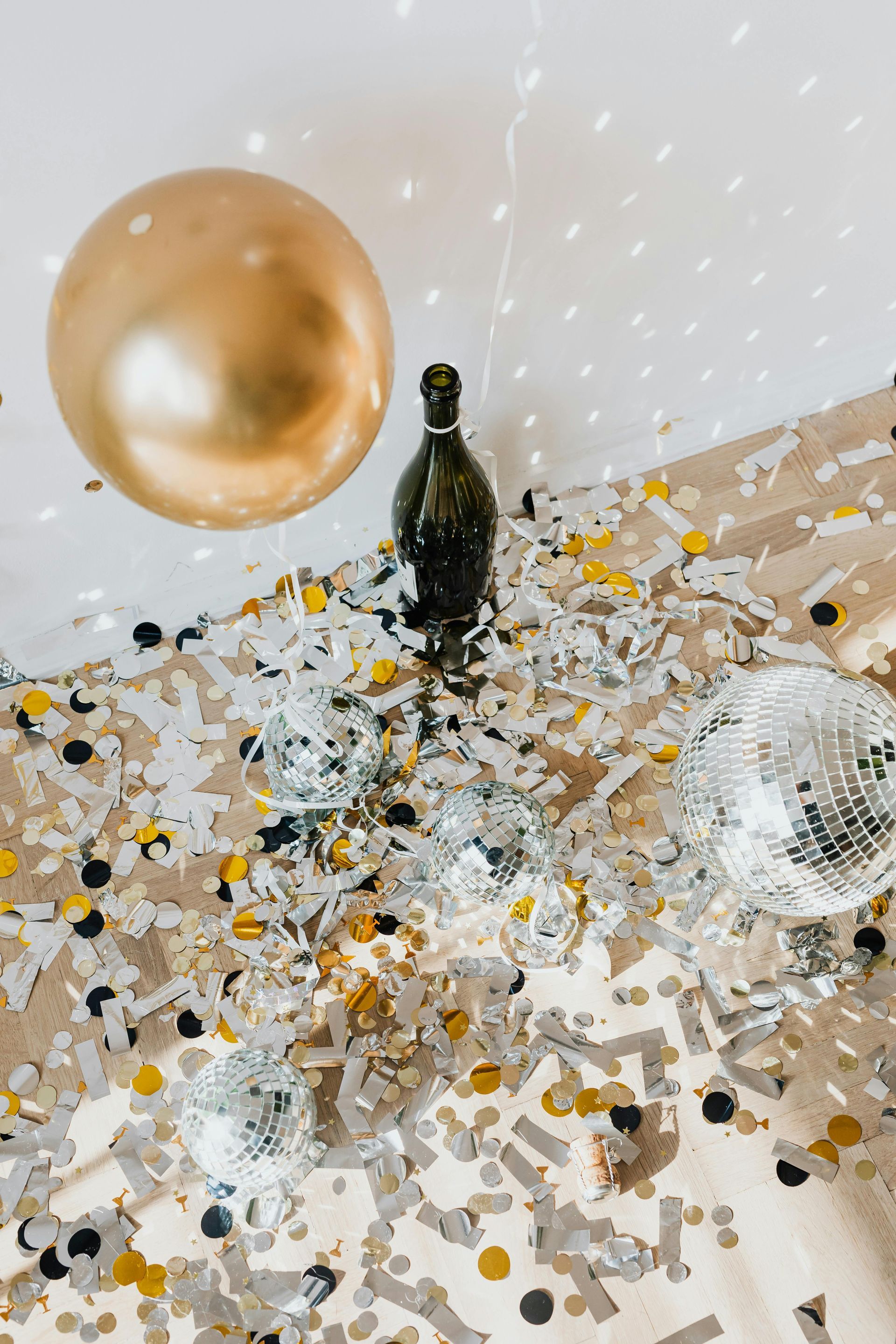 A bottle of champagne is sitting on a table surrounded by confetti and balloons.