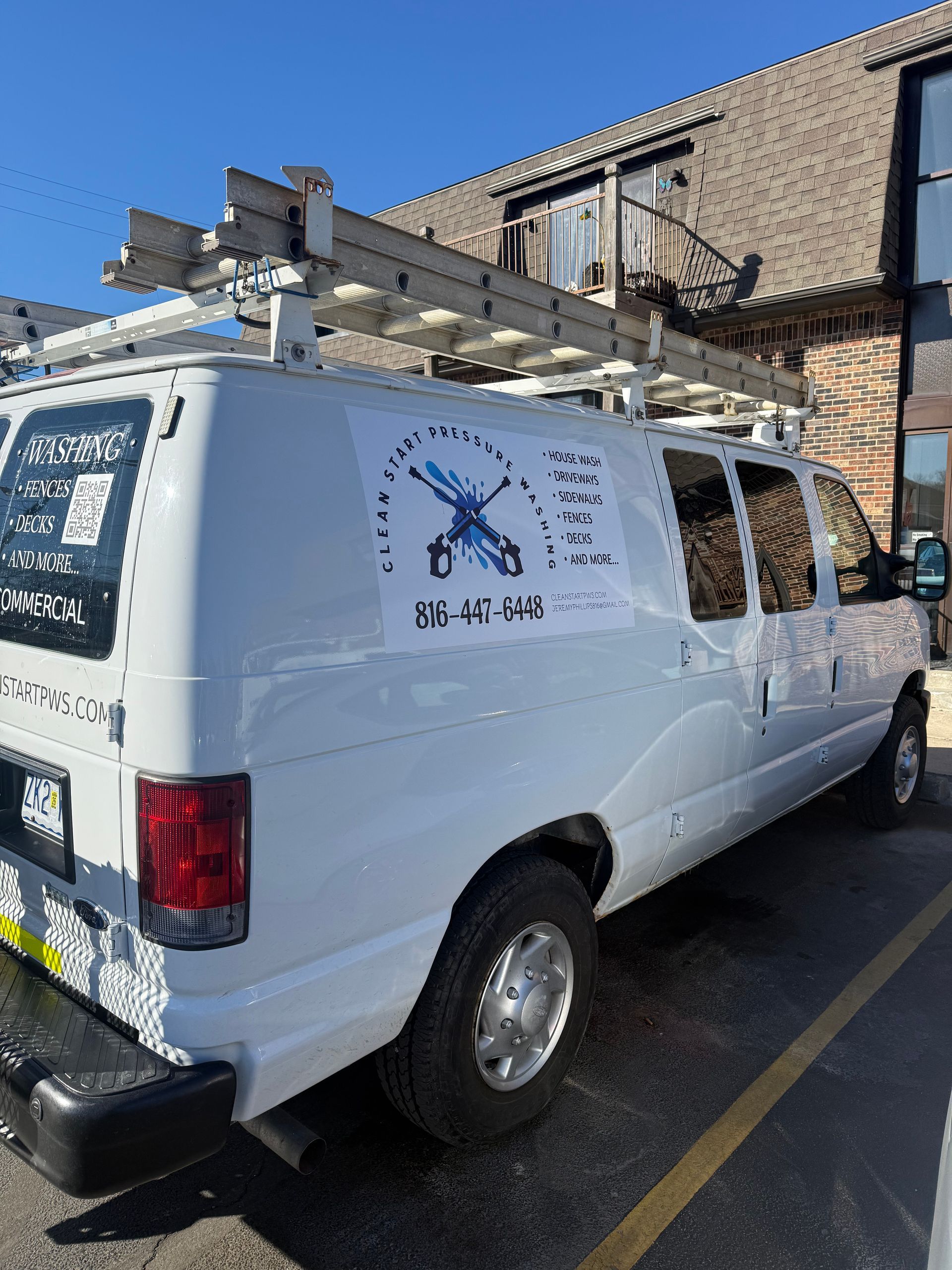 A white service van with a ladder rack parked outside a brick building, featuring a logo of crossed tools on its side.