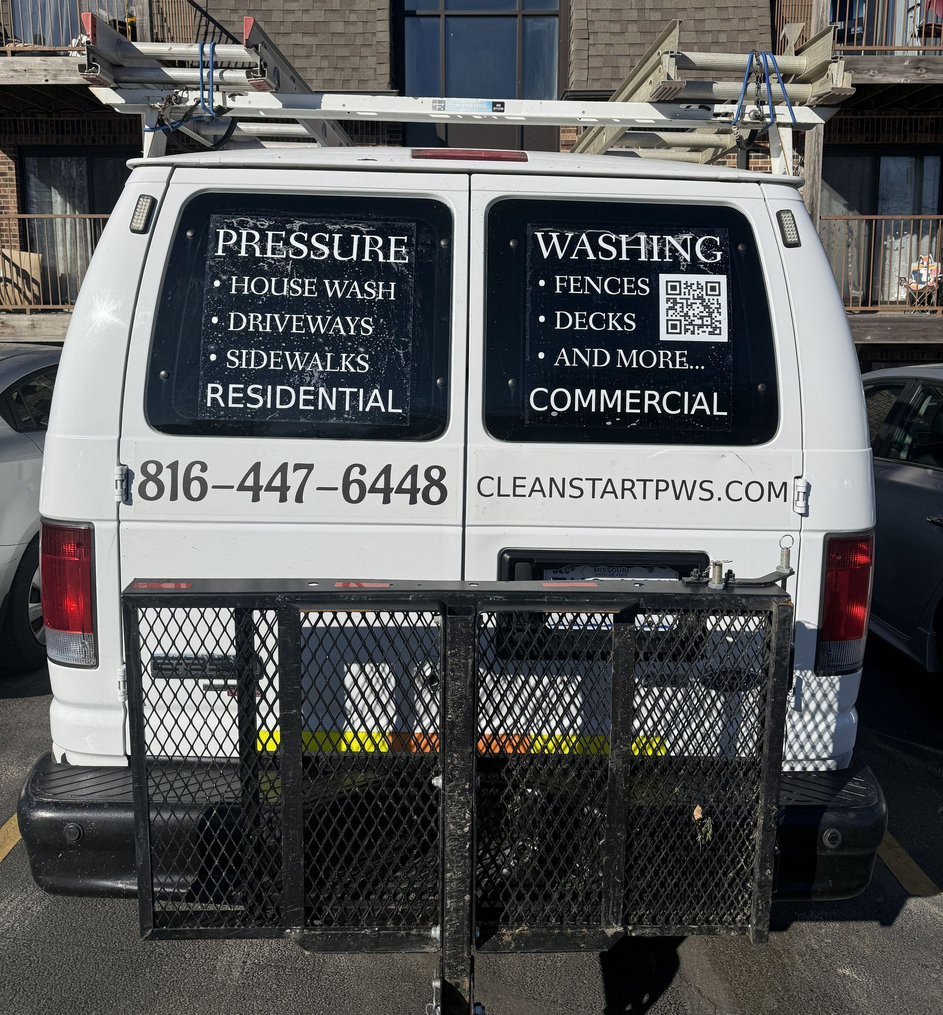 A white van parked outdoors advertising pressure washing services with a phone number and website displayed on the rear.