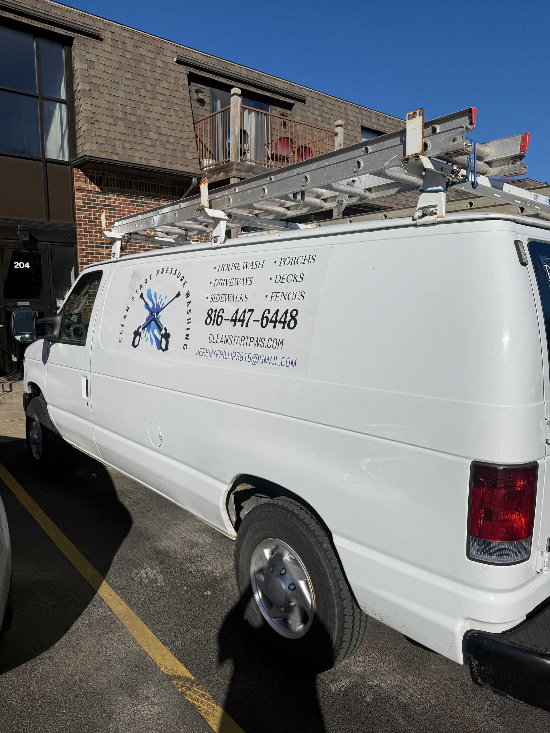 A white work van parked outdoors with a ladder on the roof and a business logo with a phone number on the side.