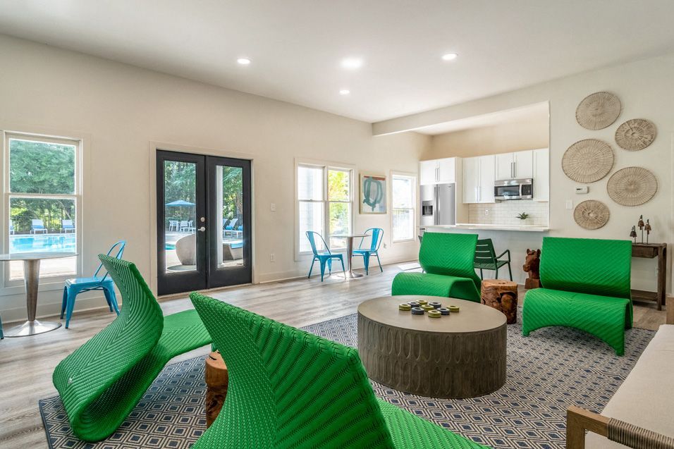 Interior view of a community lounge area with green chairs and kitchen.