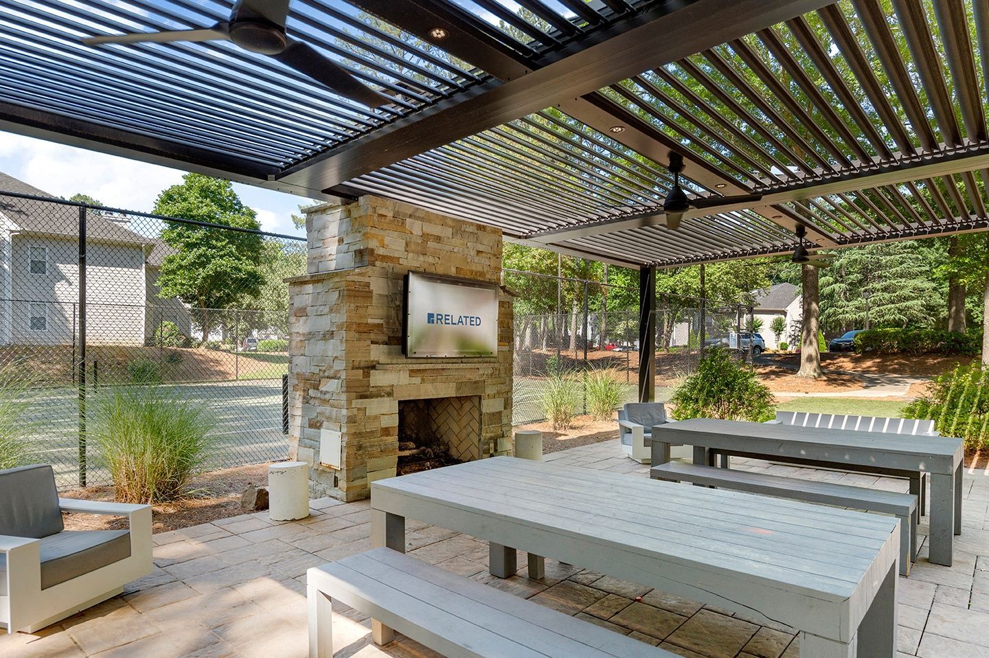 Outdoor gathering area with stone fireplace and tables under a shaded structure.