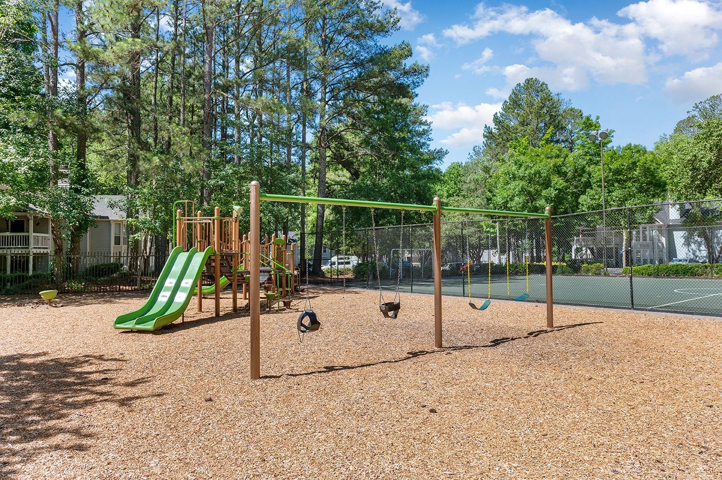 Children's playground with slides and swings in a grassy area surrounded by trees.
