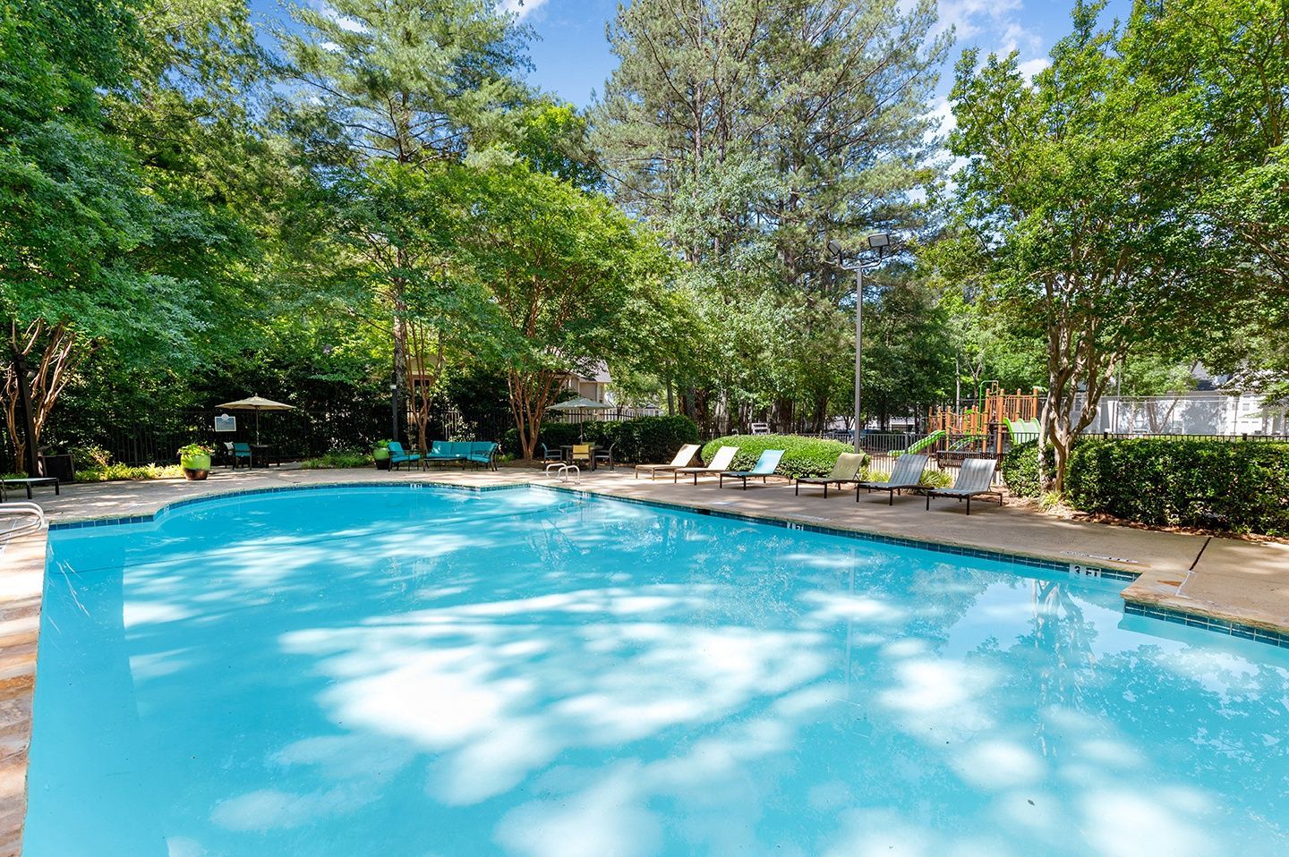 Outdoor community pool surrounded by trees and lounge chairs