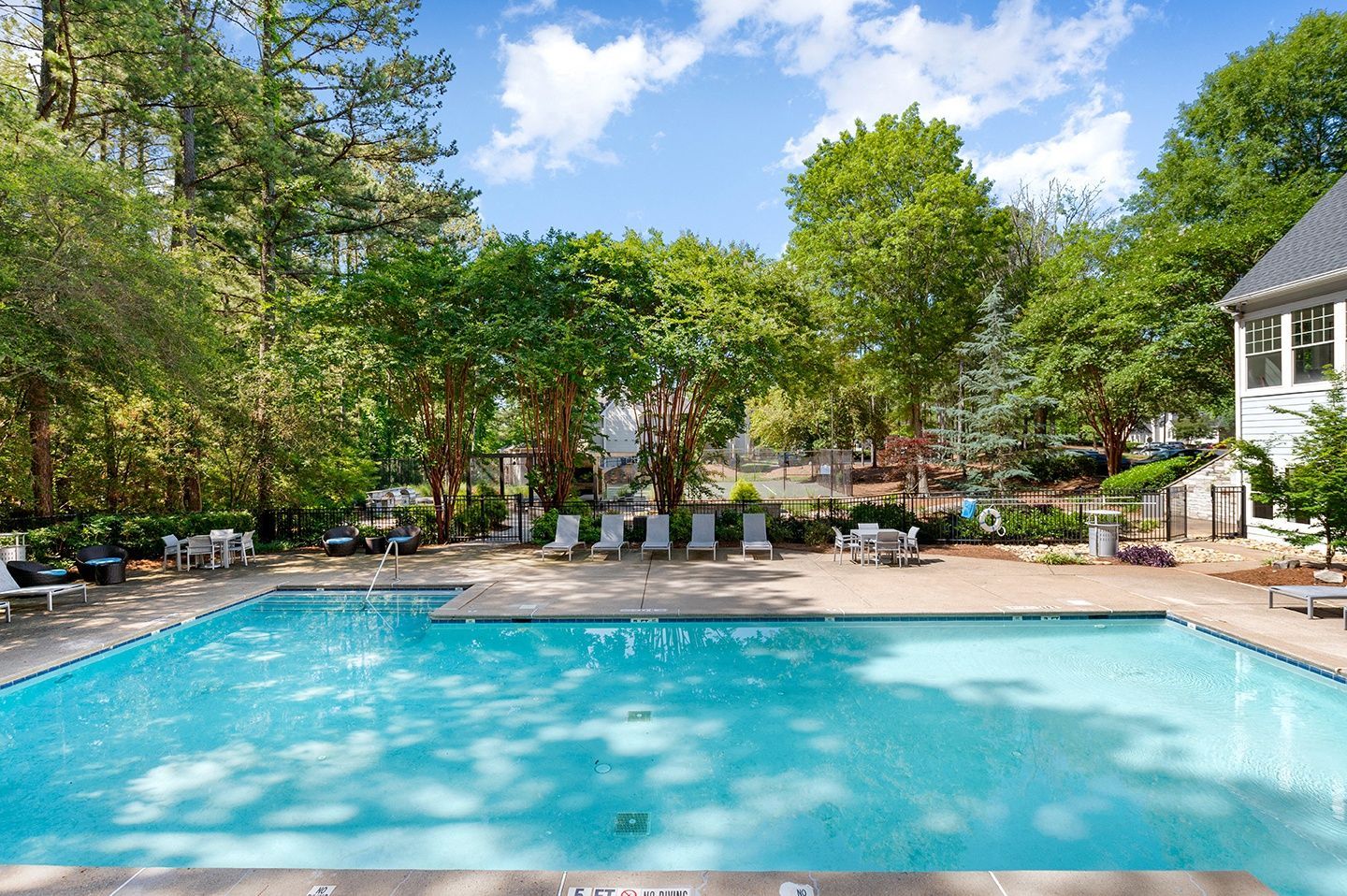 Outdoor community pool surrounded by greenery and lounge chairs.