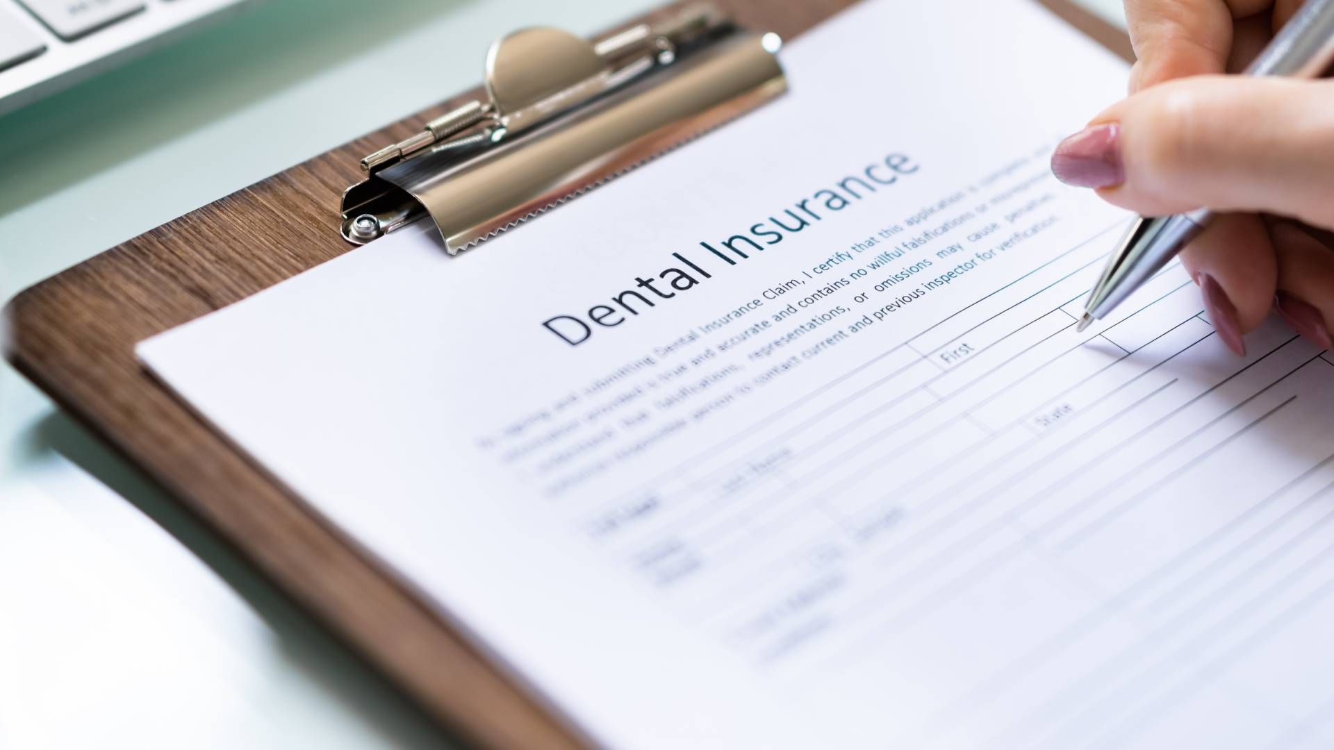 Person filling out a dental insurance form on a clipboard with a pen.