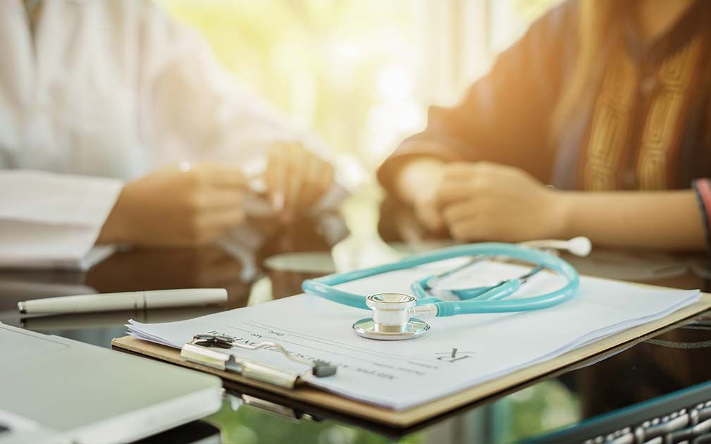 Doctor and patient at desk; stethoscope on clipboard with medical form.